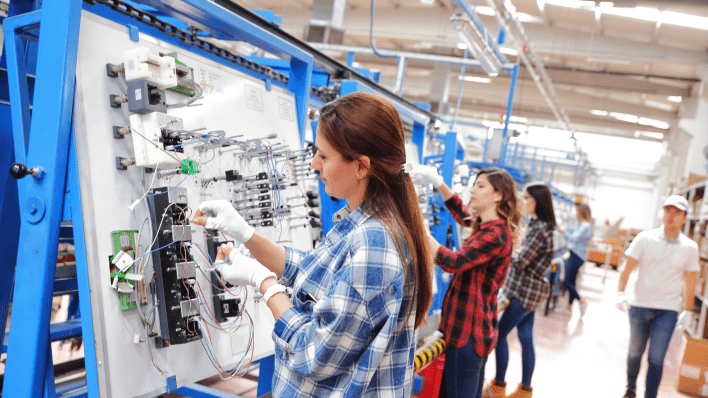 Tres mujeres con camisas a cuadros trabajando en una cadena de ensamblaje de electrónica