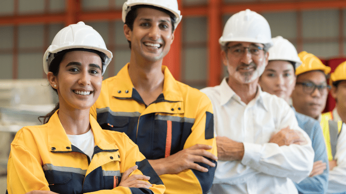 Cinco trabajadores y trabajadoras con cascos y los brazos cruzados, sonriendo a la cámara.