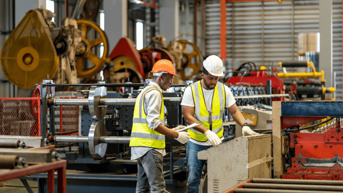 Trabajadores en una línea de ensamblaje en una fábrica, concentrados en sus tareas con maquinaria y equipos a su alrededor.